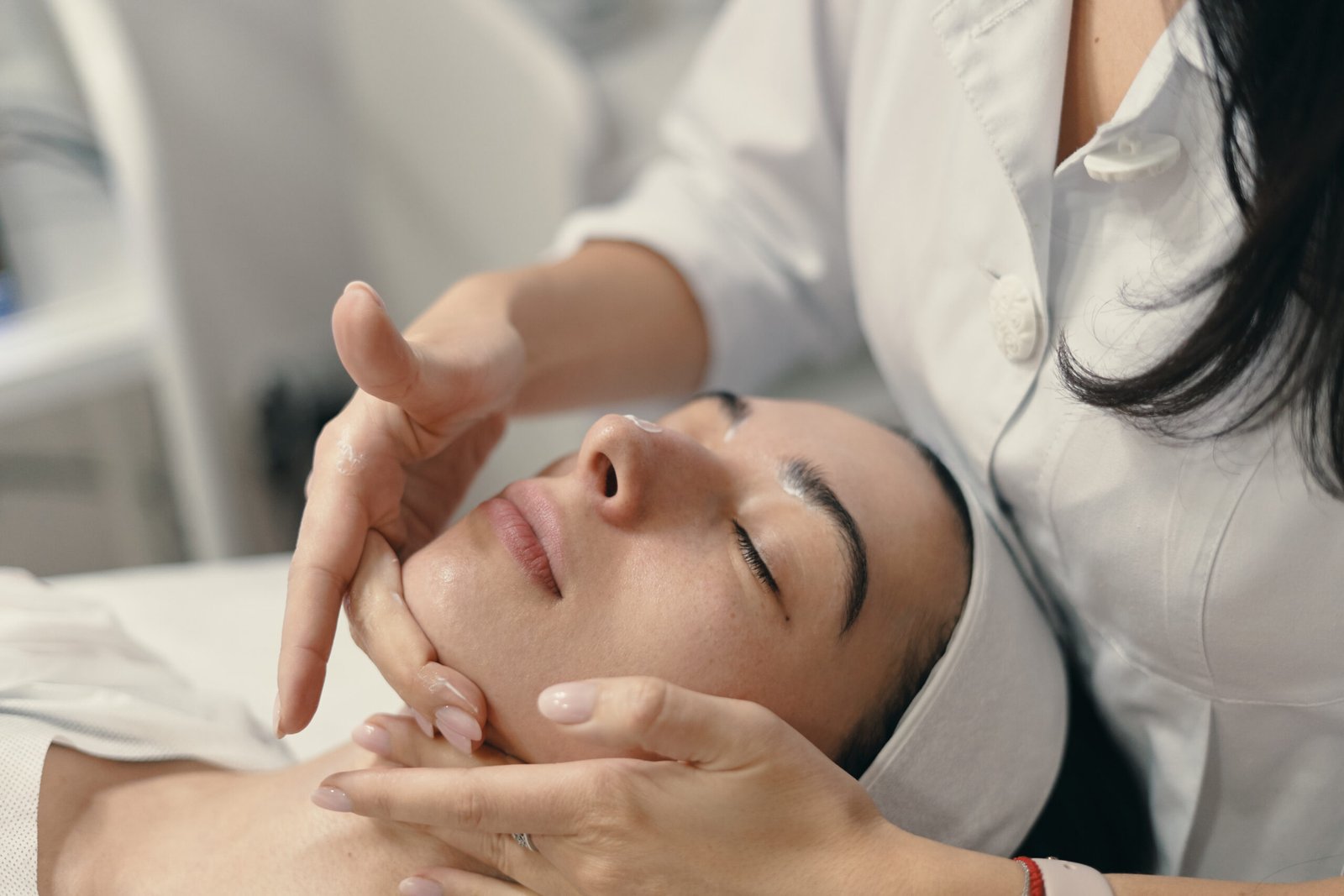 Beauty, spa and cosmetology concept. Young woman lies with closed eyes, cosmetologist making procedure for facial skin rejuvenation, facial massage.